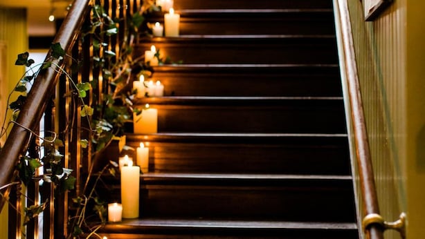 Una escalera de madera con barandilla decorada con follaje e iluminada por velas.
