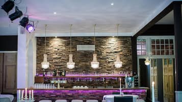 Un área de bar con un fondo de pared de piedra, varios candelabros colgantes y una barra con distintos botellas y vasos.