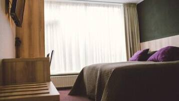 A hotel room with a bed, a wooden desk, and a window with curtains.