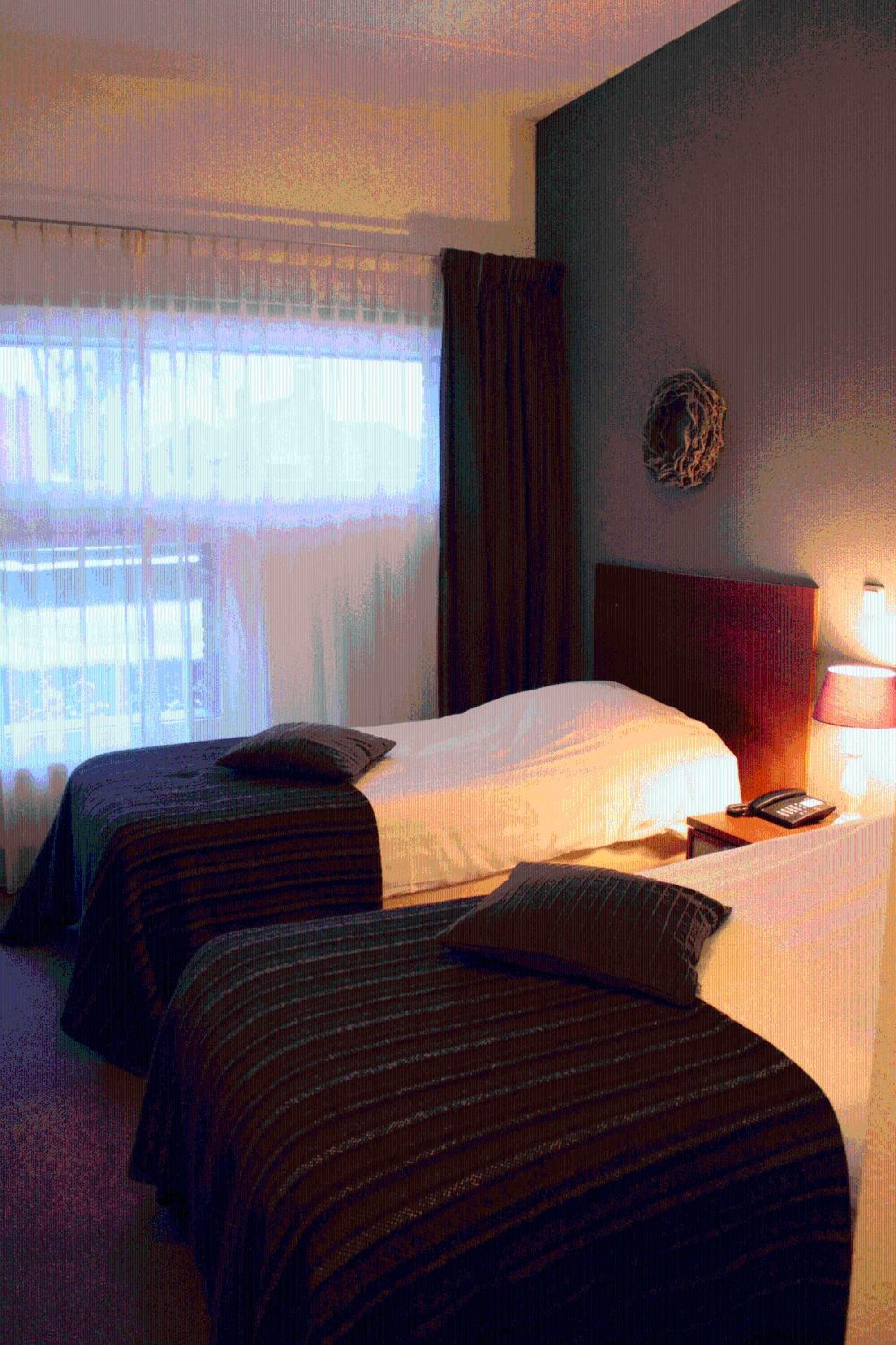 Een hotelkamer met twee bedden, een nachtkastje, een lamp en een raam met gordijnen.