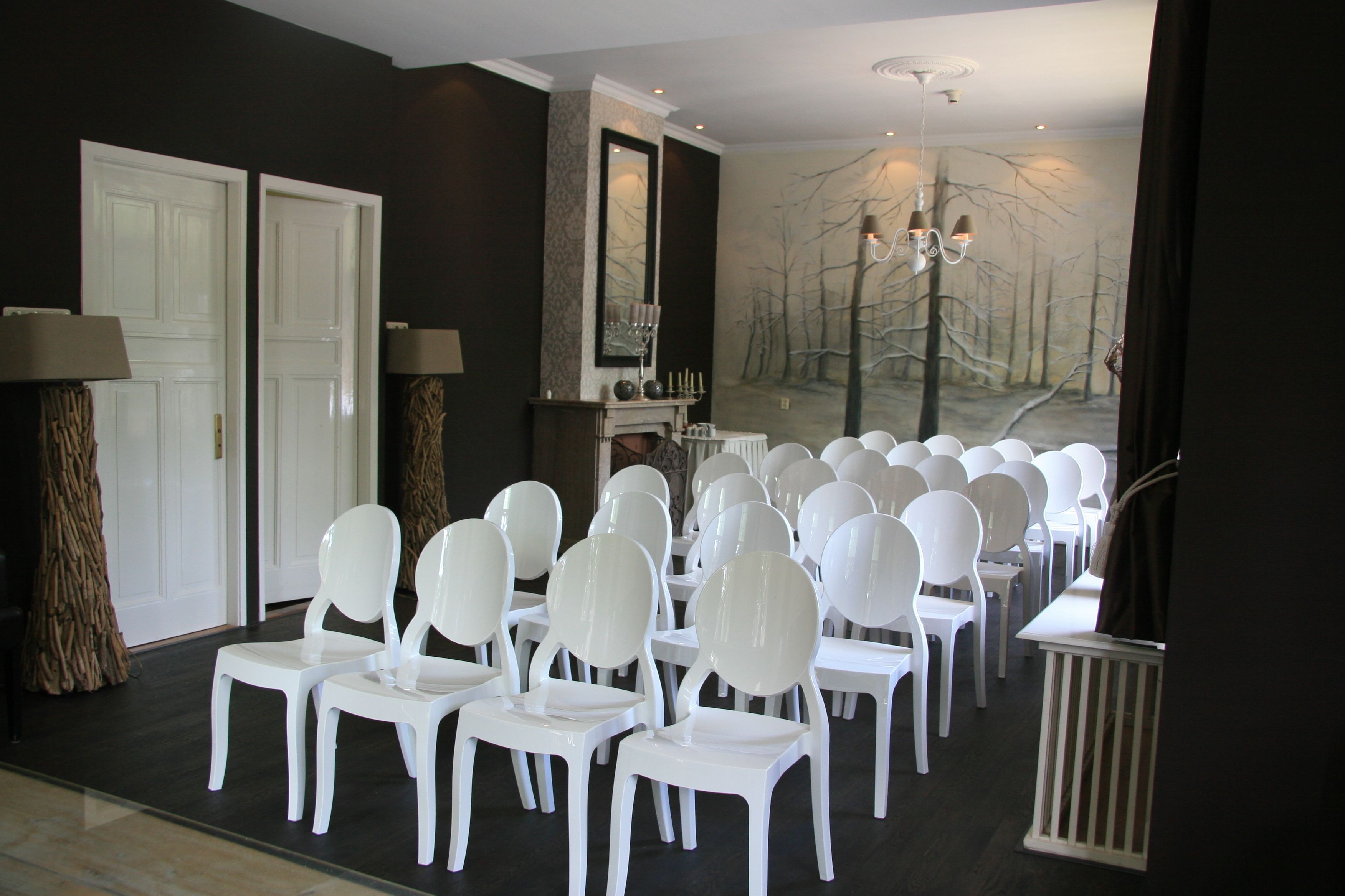 Une pièce avec des chaises blanches disposées en rangées, une cheminée et un grand miroir au mur.