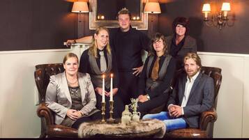 Een groep mensen zit op een leren bank met een bont plaid, een tafel met kaarsen en wandlampen.