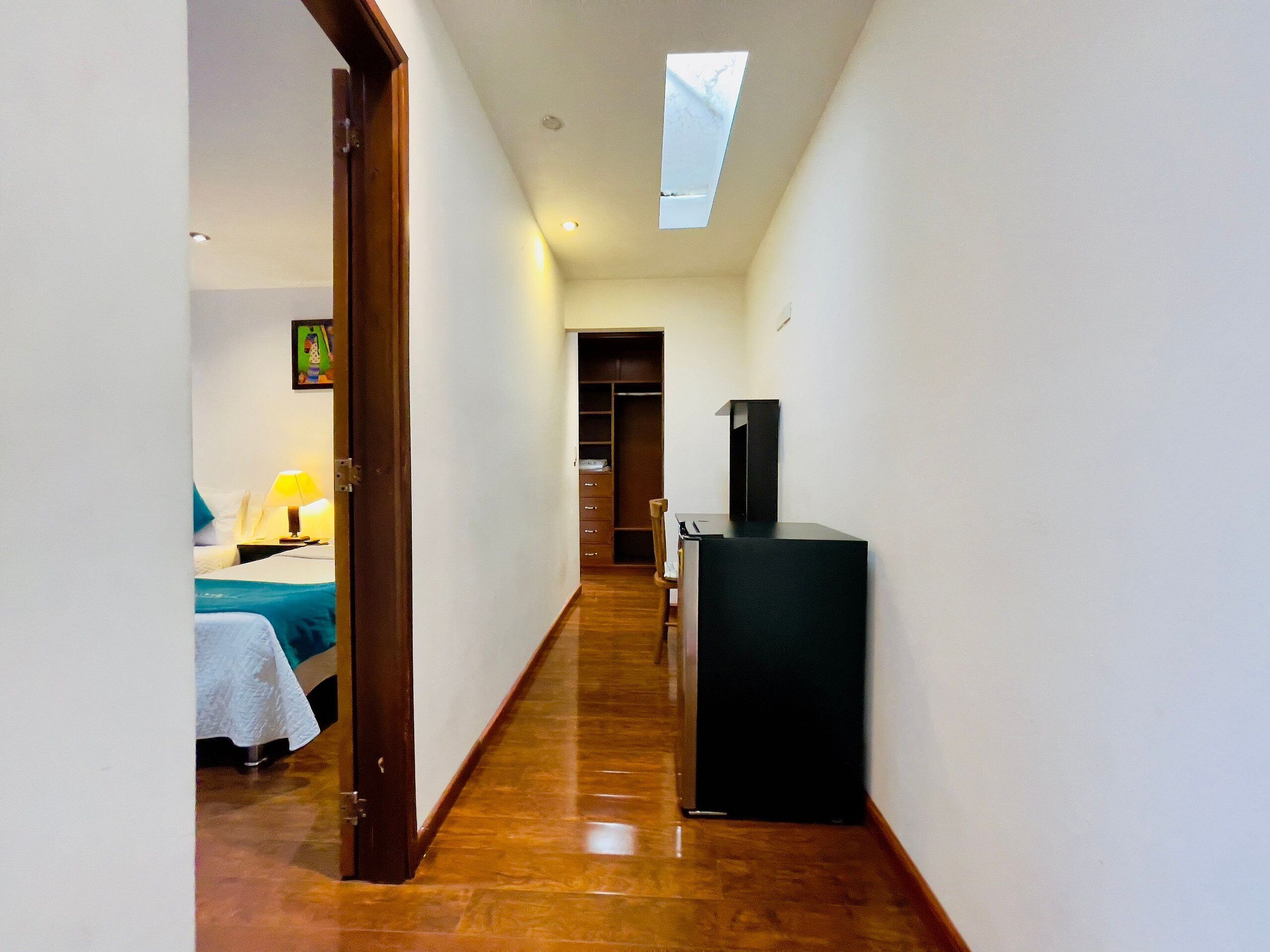 Un couloir étroit avec un lit sur la gauche, un bureau avec une lampe et un téléviseur sur la droite.
