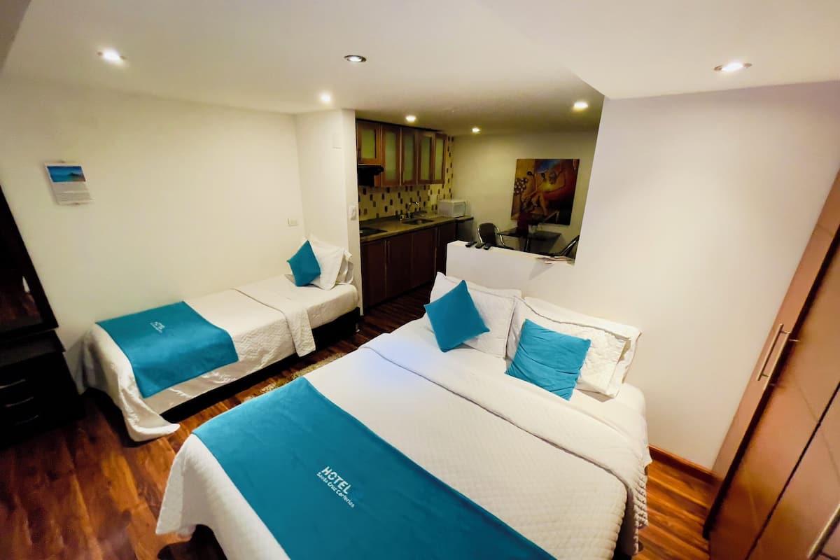 A hotel room with two beds, a kitchenette, and a small bathroom.