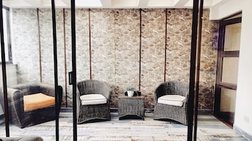 Una habitación con pared de piedra, dos sillas de mimbre con cojines, una mesita con una planta y suelo de madera.