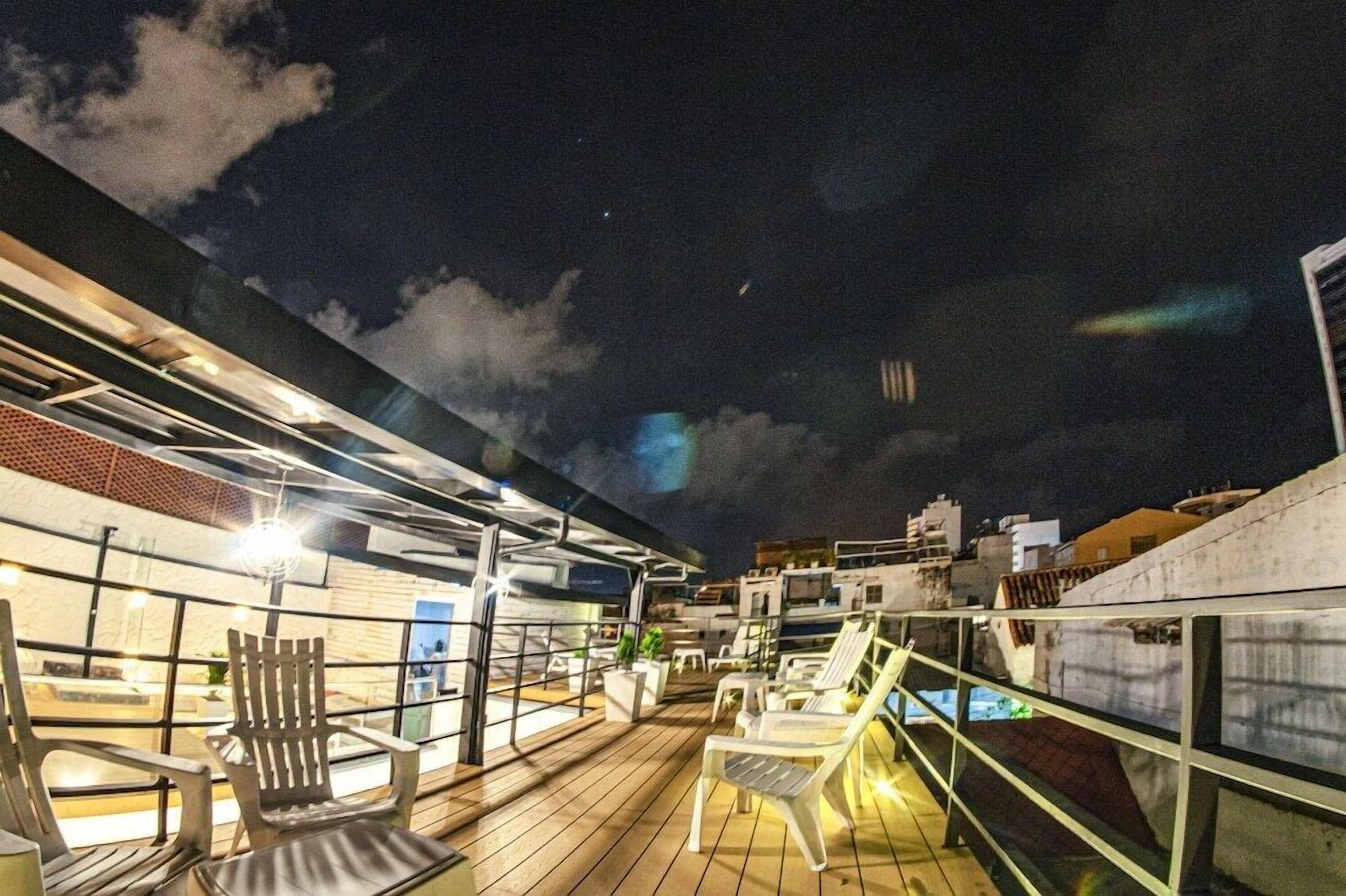 Une terrasse sur le toit, avec des sièges en plein air et une vue sur les toits de la ville illuminés la nuit.