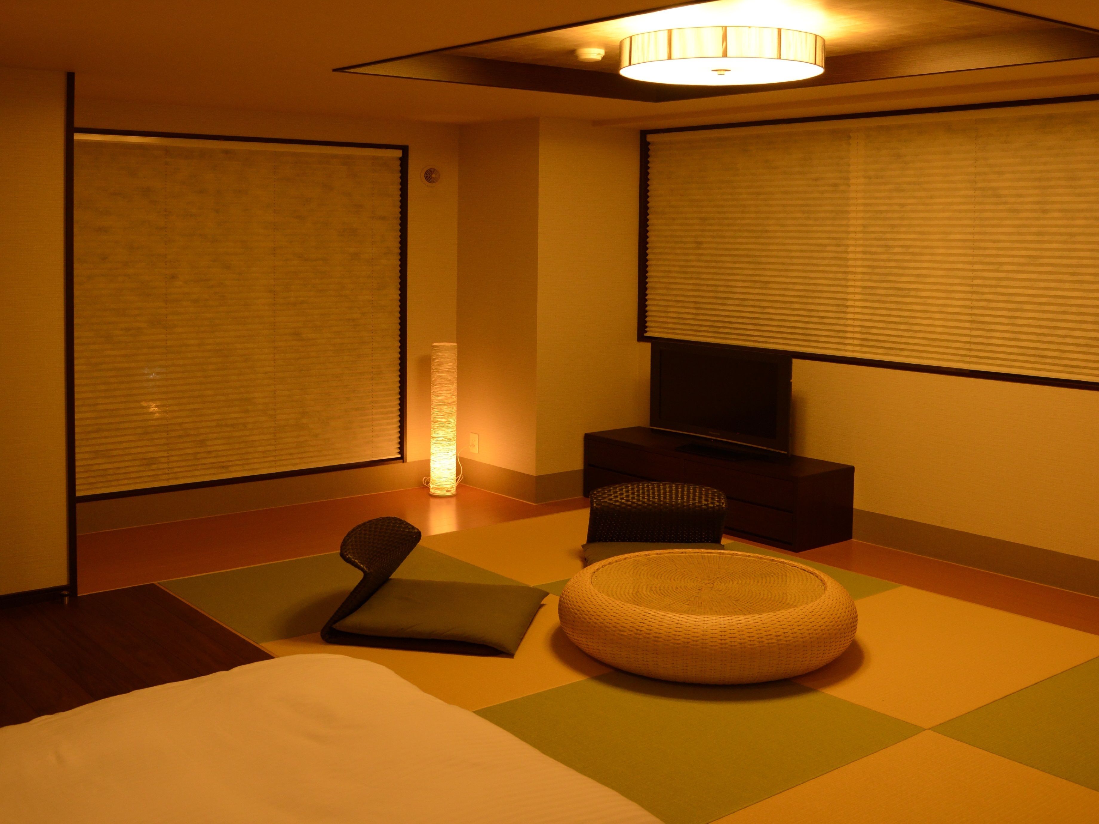 A modern hotel room with a bed, a small seating area, a television, and a lamp.