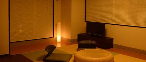 A modern hotel room with a bed, a small seating area, a television, and a lamp.