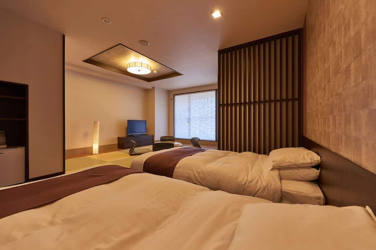Une chambre d’hôtel moderne équipée de deux lits, d’un bureau avec une chaise, d’une télévision et d’une grande fenêtre.