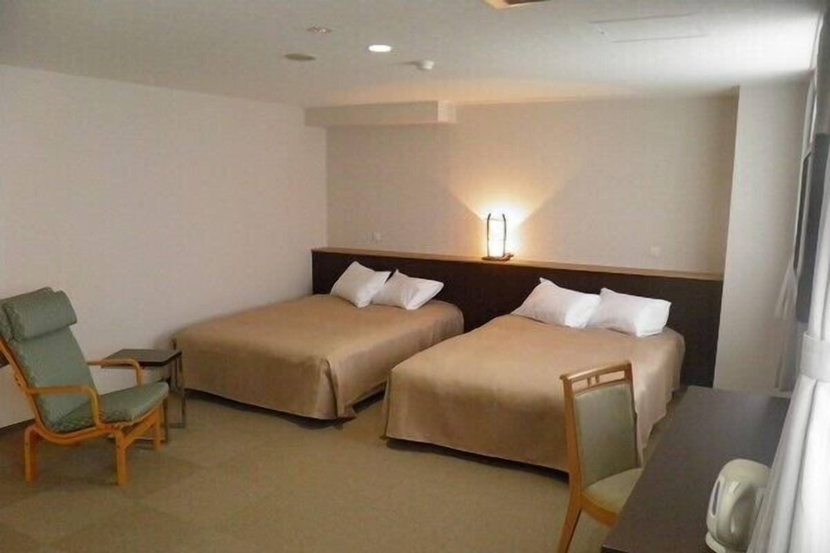 Une chambre d’hôtel avec deux lits, un bureau, une chaise et une lampe.