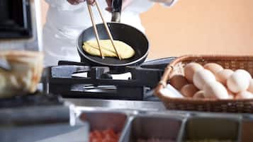 A person cooking a pancake on a griddle, with a basket of eggs and containers of ingredients nearby.