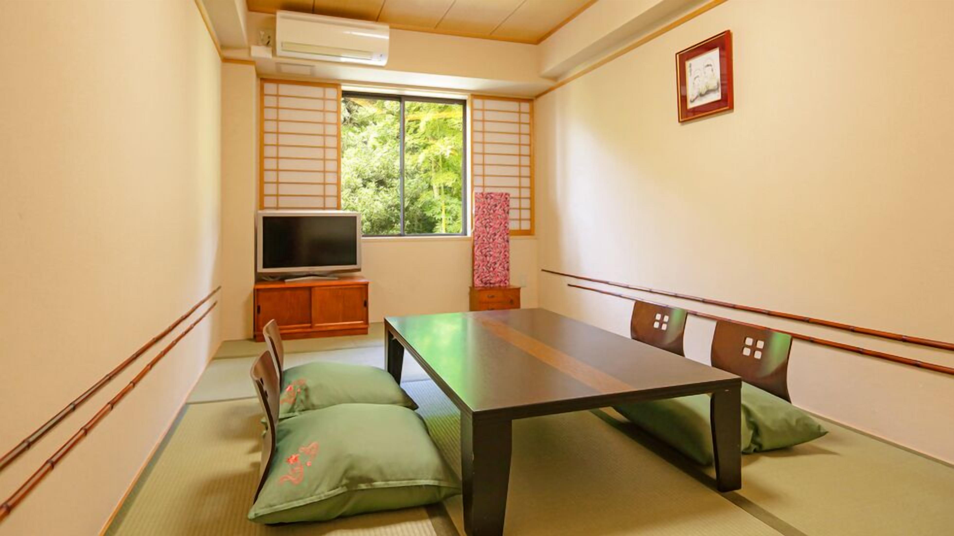 Een traditionele Japanse kamer met tatami vloerbedekking, een lage tafel, kussens, een televisie en een raam met uitzicht op groen.