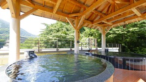 Un área de aguas termales al aire libre con techo de madera, una balsa de piedra circular y barandilla de metal.