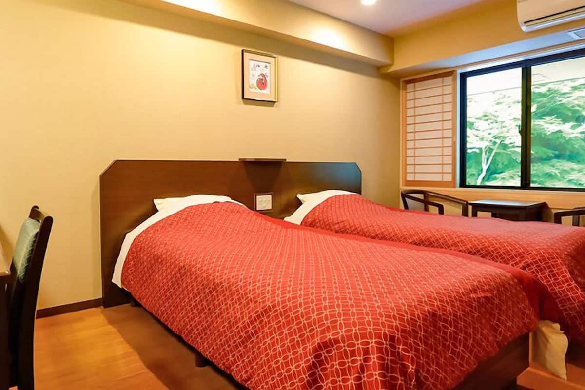 Habitación de hotel con dos camas, un escritorio, una silla, un televisor y una ventana con vistas.