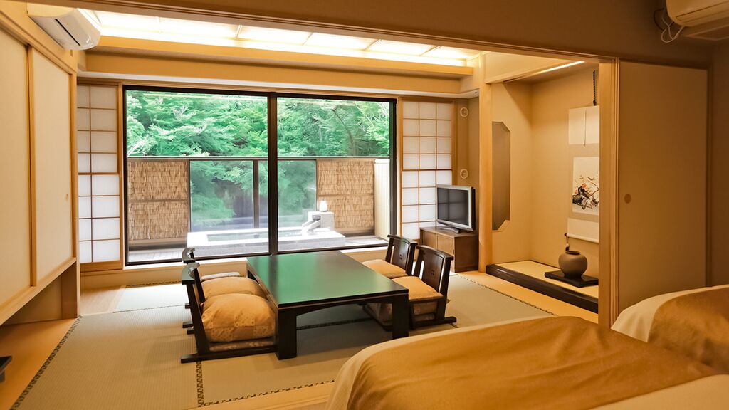 A traditional Japanese-style room with tatami flooring, a low table with cushions, a television, and a sliding door leading to a balcony.