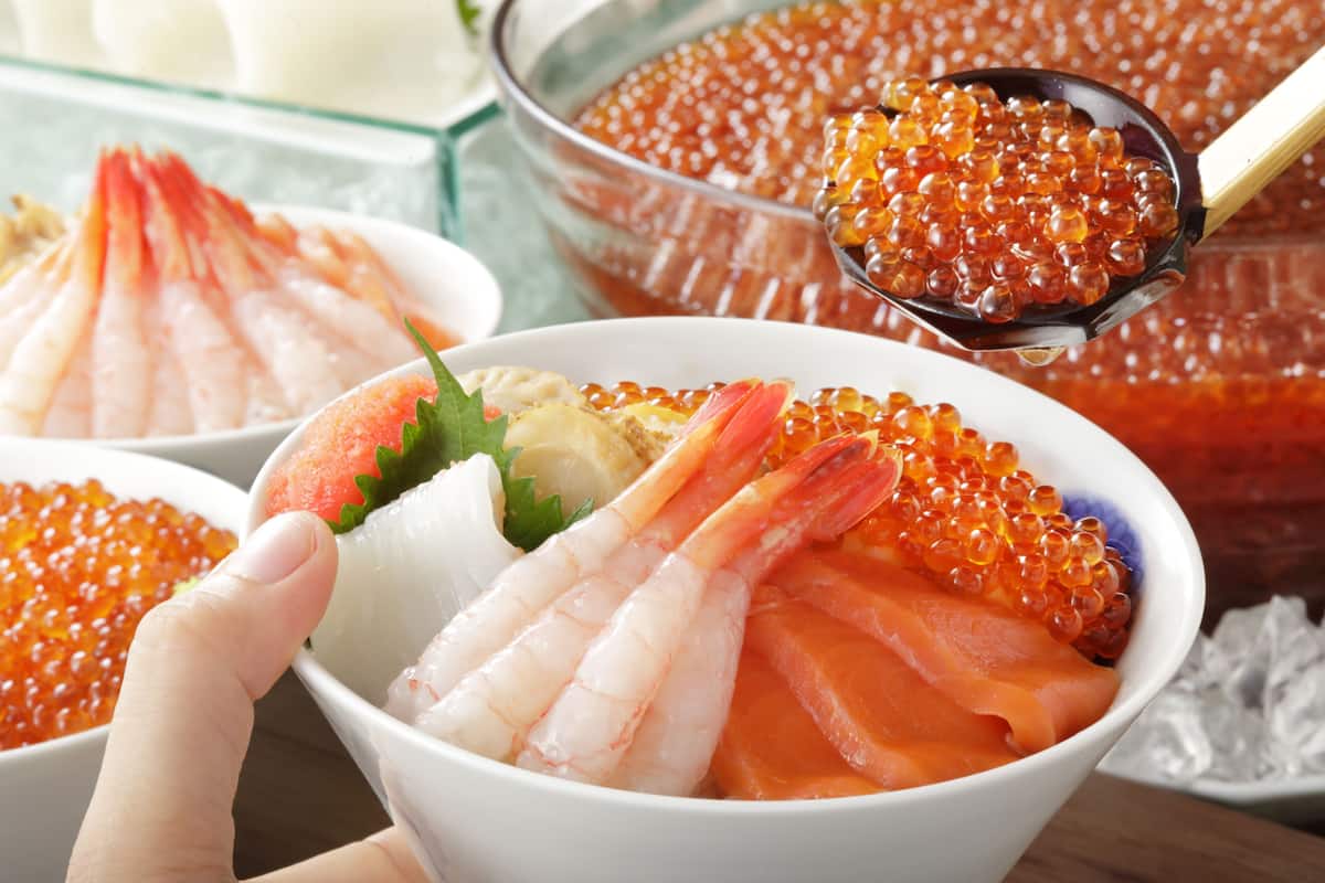 Un tazón de sushi con camarones y salmón, y una cucharada de huevas de salmón.
