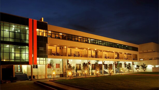 Um edifício moderno com vários andares, grandes janelas e uma área de entrada bem iluminada.