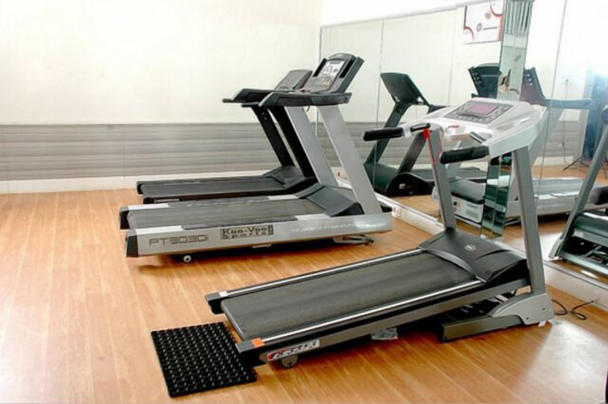 Three stationary treadmills in a room with wooden flooring and a mirrored wall.