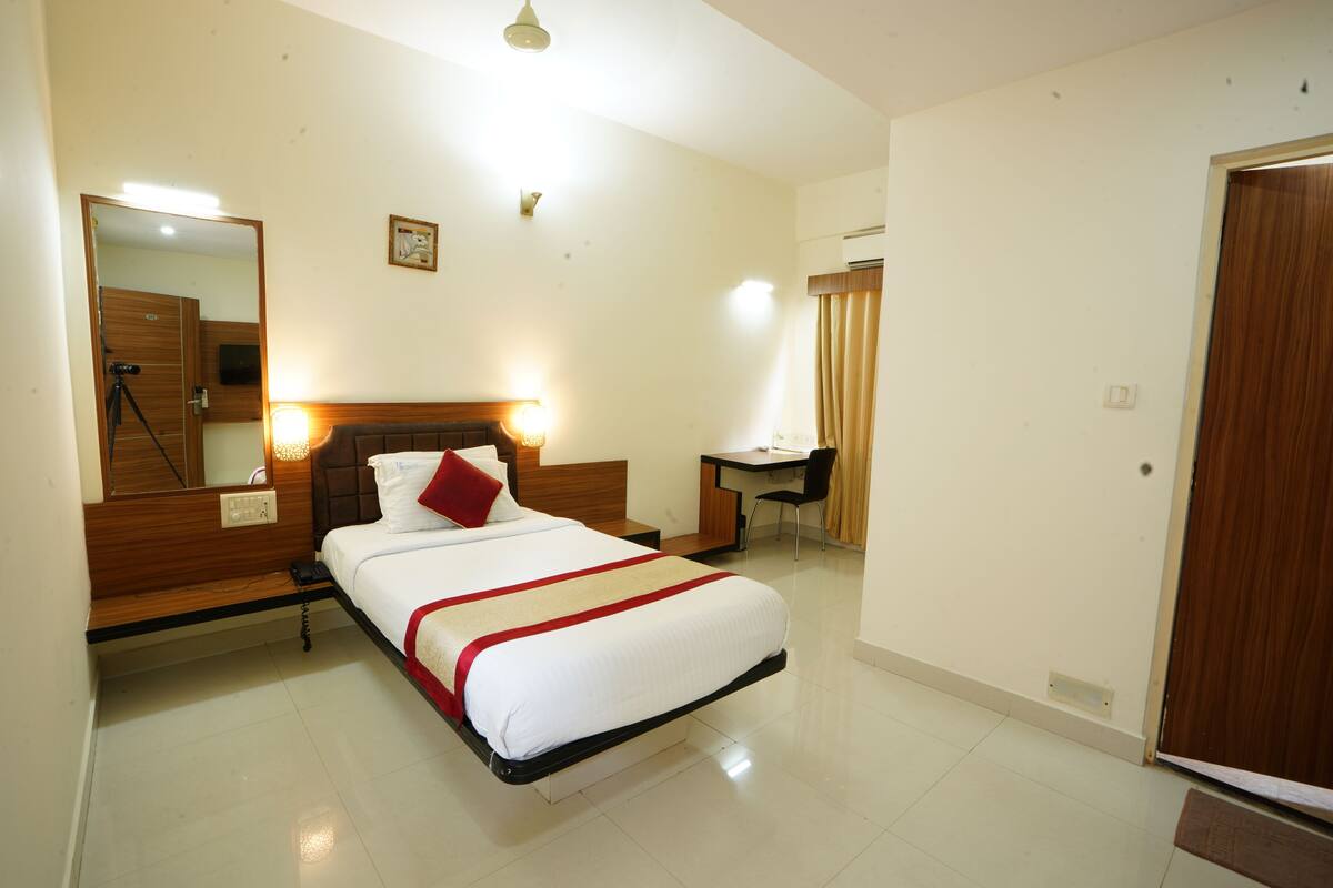 A hotel room with a bed, a desk, a chair, a mirror, and a door.