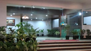 Un vestíbulo de hotel con una escalera que conduce a una recepción. Se observan plantas en macetas y un candelabro.