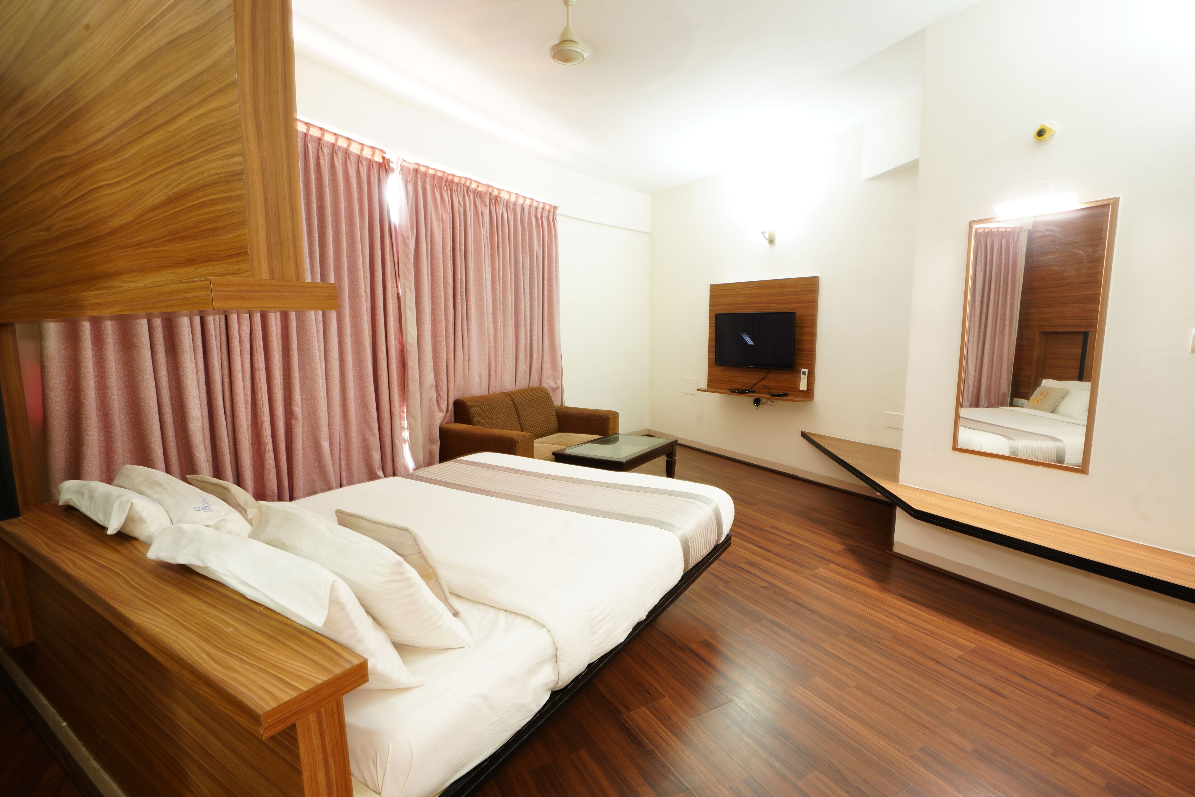 Ein Hotelzimmer mit einem großen Bett, einem Sessel, einem kleinen Tisch, einem Fernseher und einem Spiegel.
