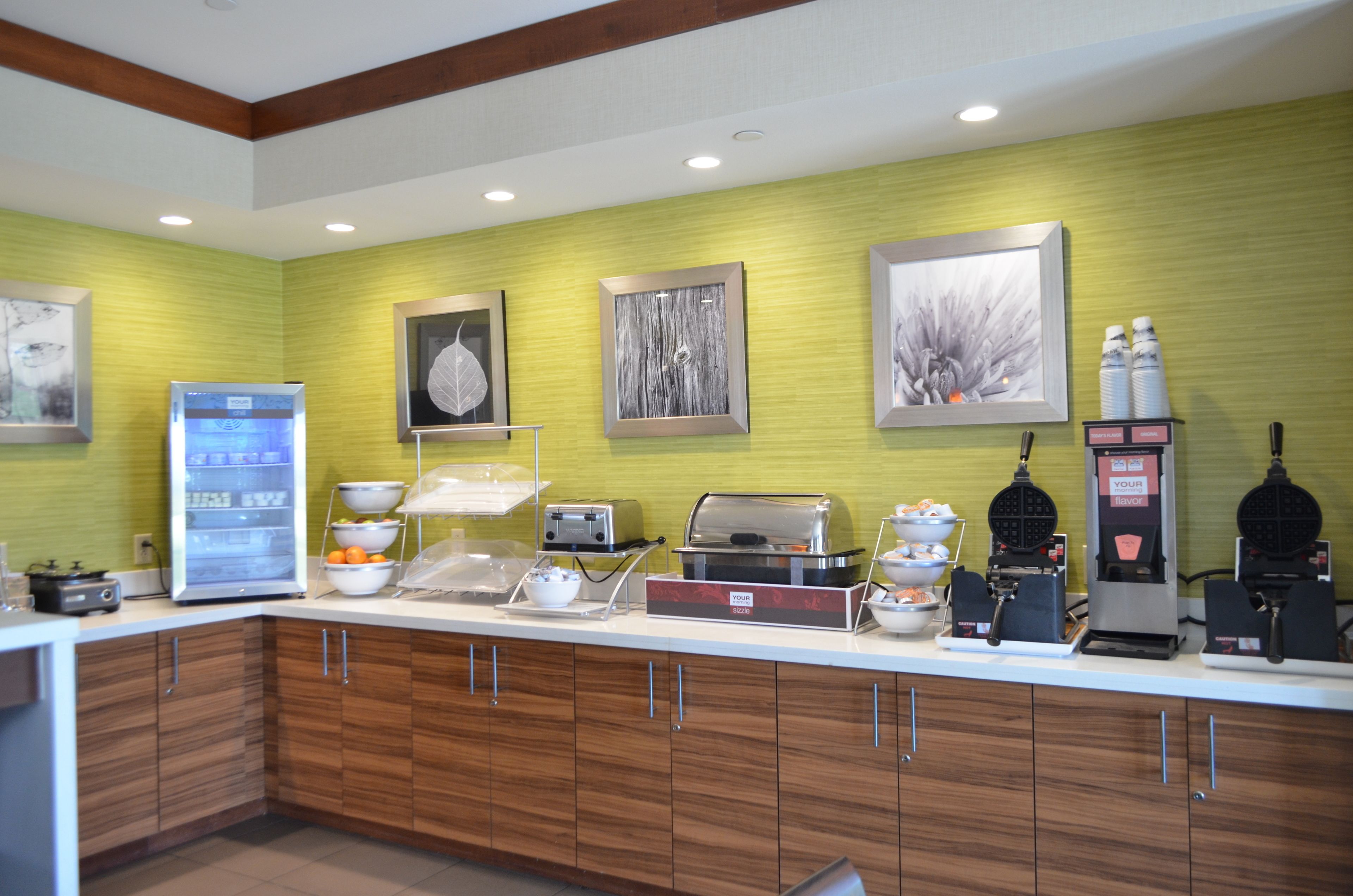 A breakfast bar with a refrigerator, toaster, waffle maker, and coffee machine.