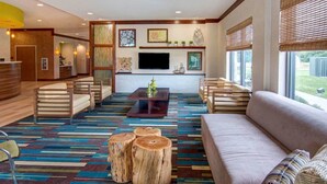 A modern living room with a sofa, chairs, a coffee table, and a TV. There is a reception desk in the background. - Comfort Suites Bossier City - Shreveport (Bossier City)