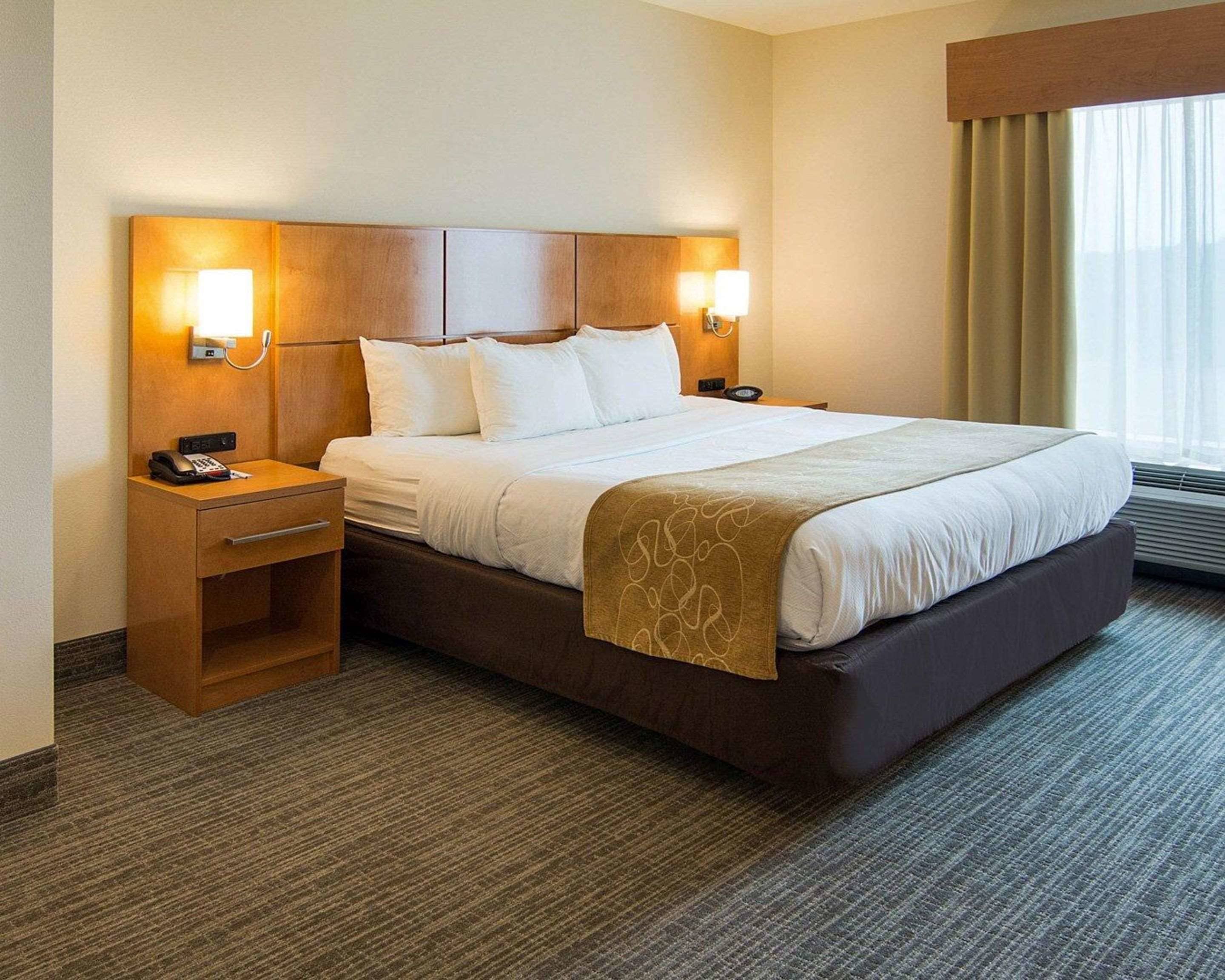 A hotel room with a large bed, two bedside tables, a desk, and a window with curtains.