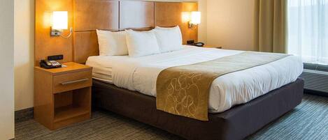 A hotel room with a large bed, two bedside tables, a desk, and a window with curtains.