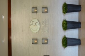A hotel lobby with a central circular sign, four wall-mounted lights, and three potted plants.