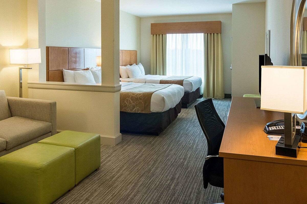 Ein Hotelzimmer mit zwei Betten, einem Schreibtisch mit Lampe, einem Sessel und einem Sofa.