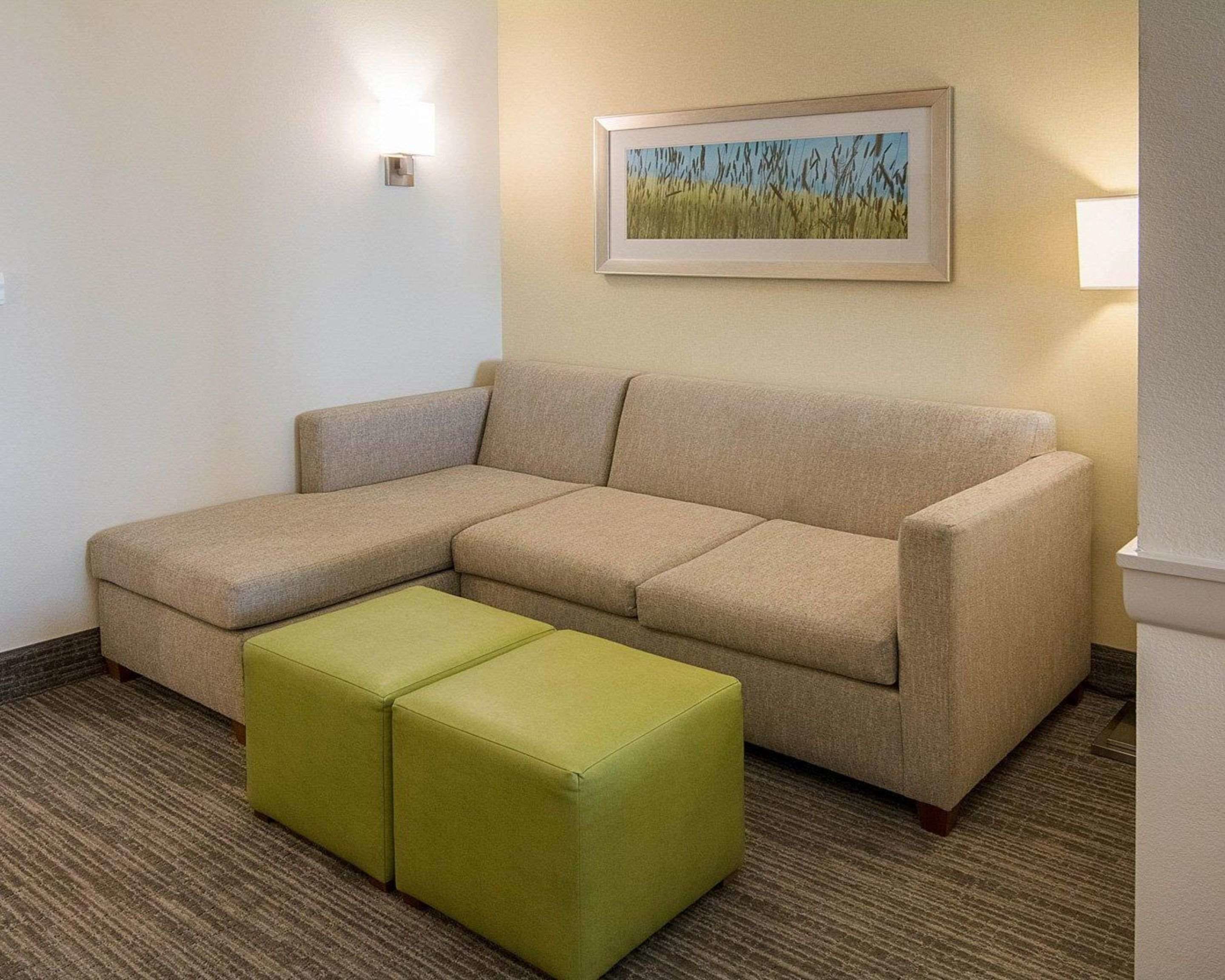 A beige sectional sofa with a green ottoman in a hotel room.