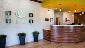 A reception area with a white brick wall, a wooden reception desk, and potted plants. - Comfort Suites Bossier City - Shreveport (Bossier City)