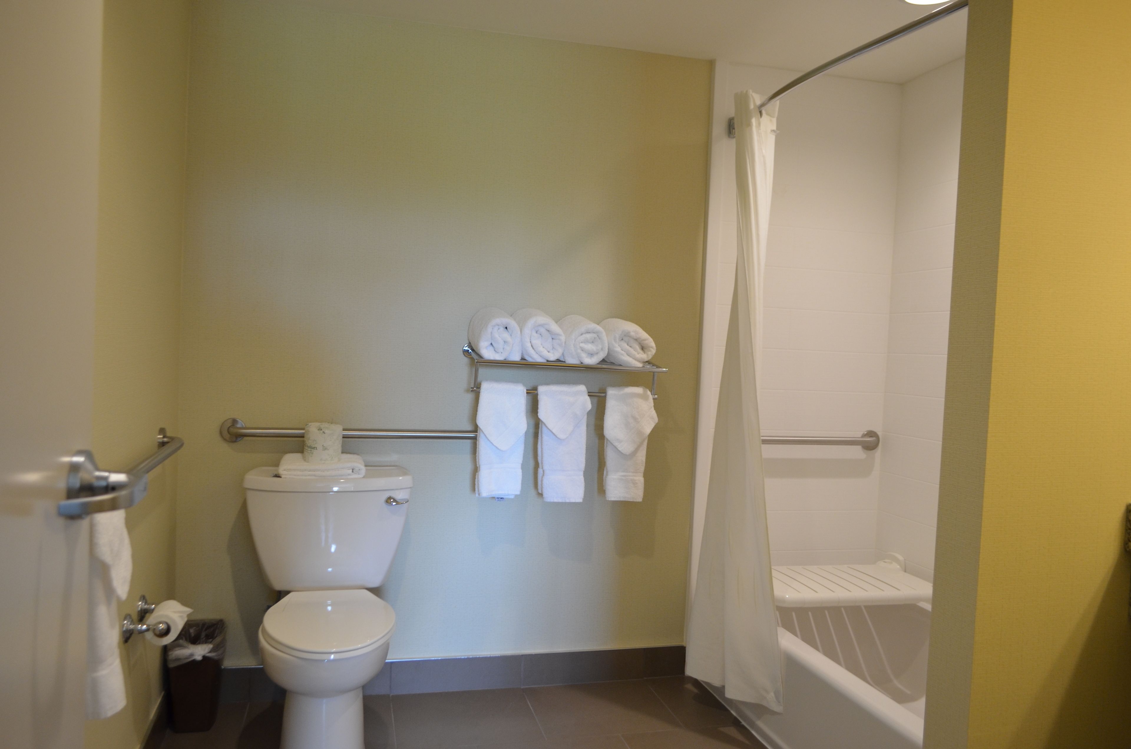 A bathroom with a toilet, a shelf with rolled towels, and a shower area.
