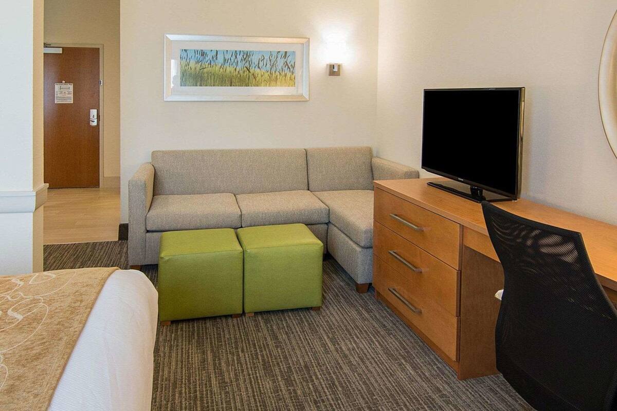 Ein Hotelzimmer mit einer Couch, einem Fernseher, einem Schreibtisch und einem Bild an der Wand.