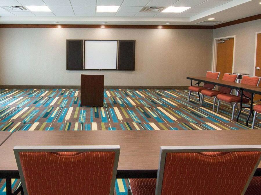 Une salle de conférence équipée d’une grande table, de nombreuses chaises, d’un pupitre et d’un écran mural.