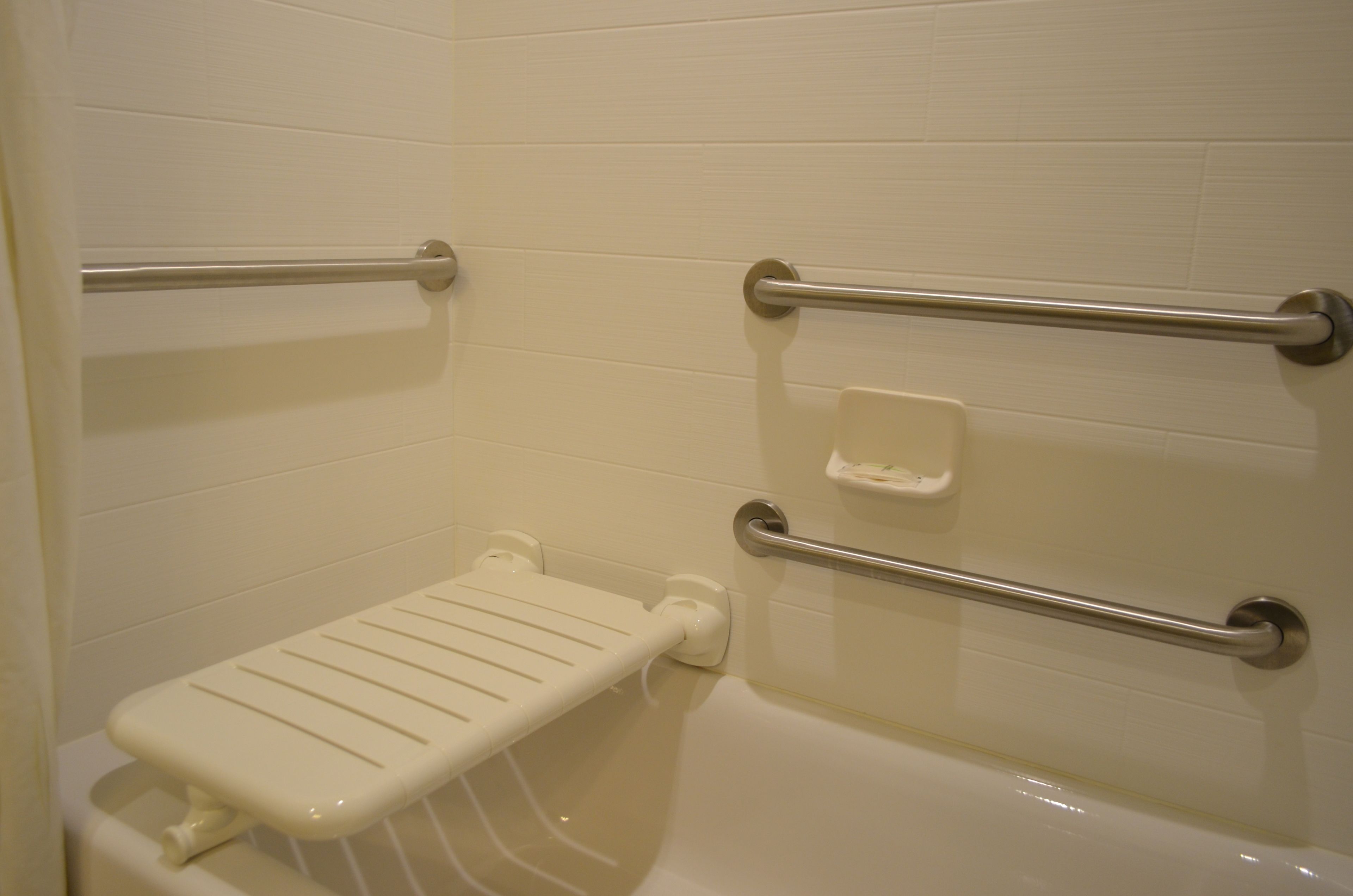 Ein Badezimmer mit einer weißen Badewanne, einer weißen Toilette und einem weißen Waschbecken. An der Wand sind zwei Haltegriffe aus Metall angebracht.