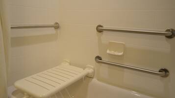 Ein Badezimmer mit einer weißen Badewanne, einer weißen Toilette und einem weißen Waschbecken. An der Wand sind zwei Haltegriffe aus Metall angebracht.