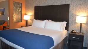 Hotellihuone, jossa on suuri sänky, kaksi yöpöytää valaisimineen, taulu seinällä ja kuviollinen tapetti.