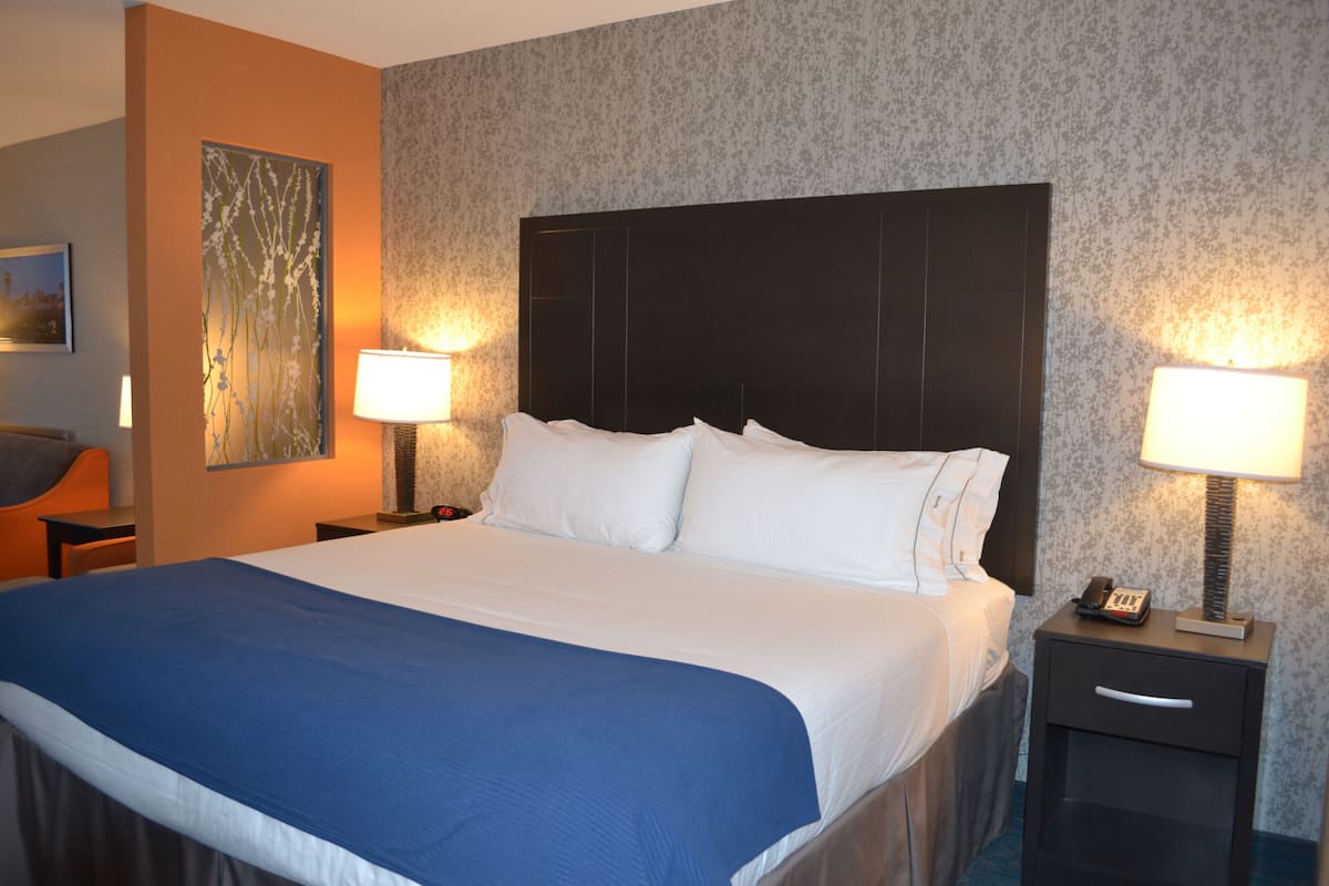 Una camera d'albergo con un letto grande, due comodini con lampade, un quadro appeso al muro e una carta da parati decorata.