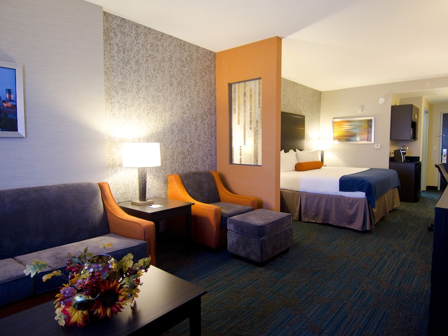 Een hotelkamer met een bank, twee fauteuils, een kleine tafel met een bloemenvaas, een bed met nachtkastje en een bureau met lamp.