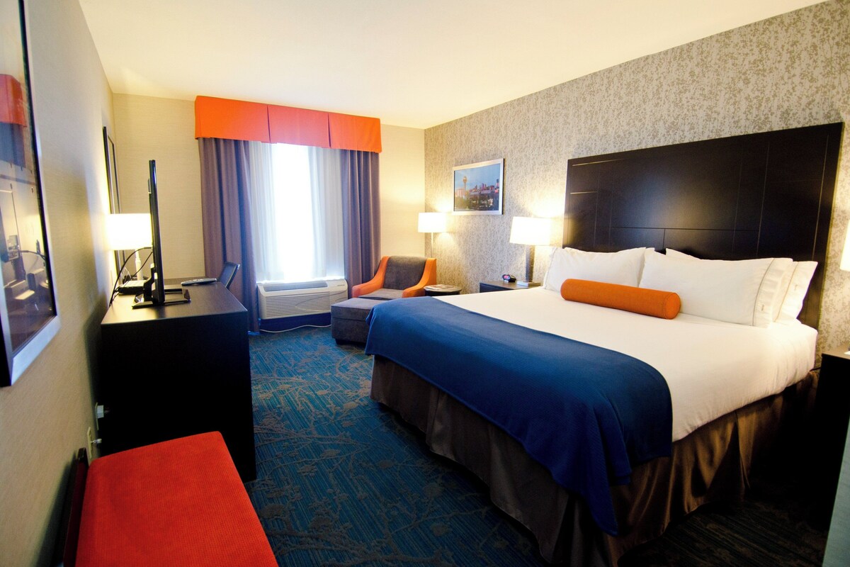Quarto de hotel com cama, duas mesas de cabeceira, escrivaninha, cadeira e janela com cortinas.