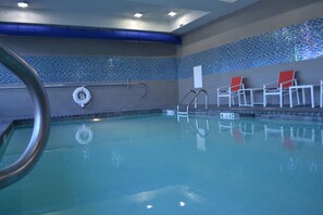 Une piscine intérieure à l’eau claire, équipée d’une bouée de sauvetage et de chaises longues rouges et blanches.
