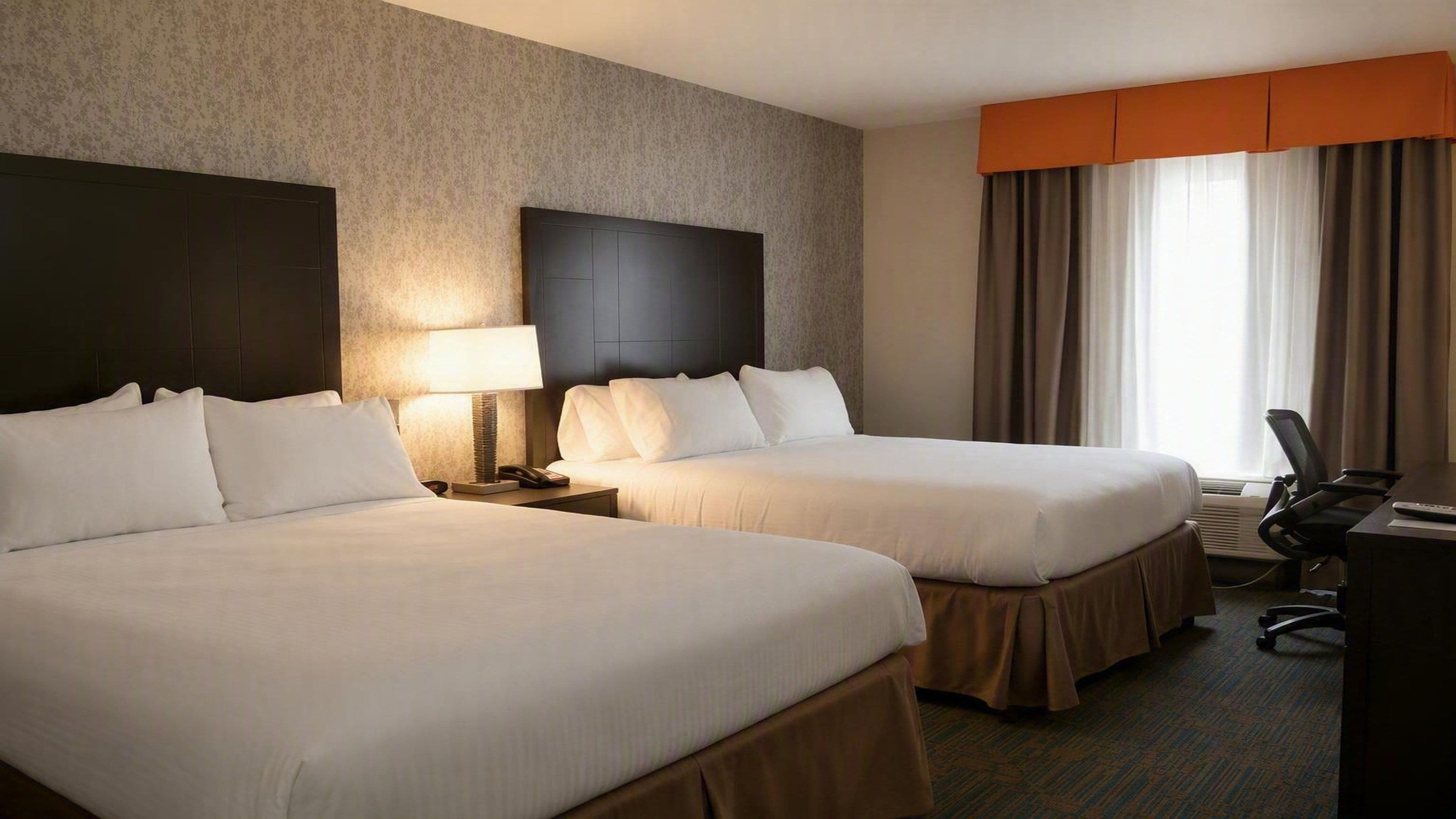 Une chambre d’hôtel avec deux lits, un bureau, une chaise et une grande fenêtre avec des rideaux.