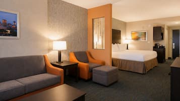 Habitación de hotel con cama, sofá, reposapiés, escritorio y silla. Se observa un cuadro en la pared y una lámpara en el escritorio.