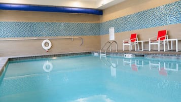 An indoor swimming pool with clear water, a lifebuoy, and red chairs.