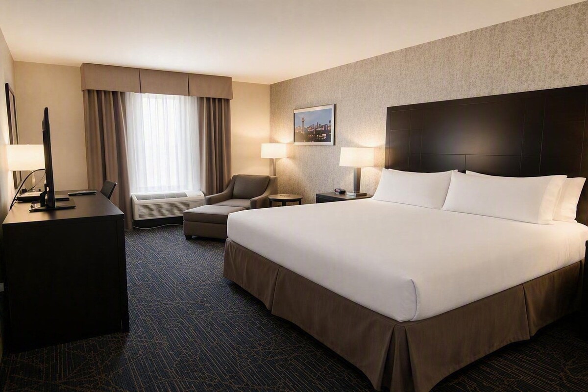 A hotel room with a large bed, a desk, a chair, and a window with curtains.