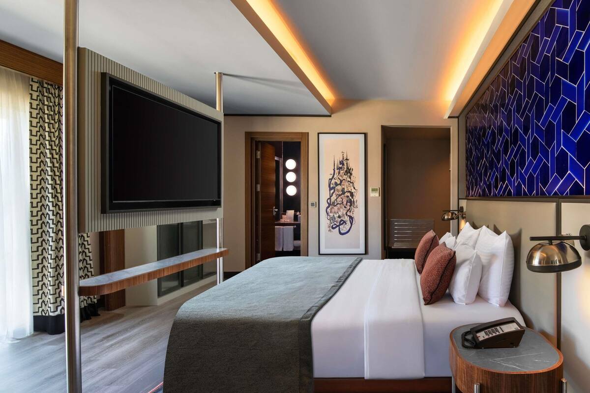 Een moderne hotelkamer met een groot bed, een flatscreen televisie, een nachtkastje met telefoon en een decoratief wandobject.