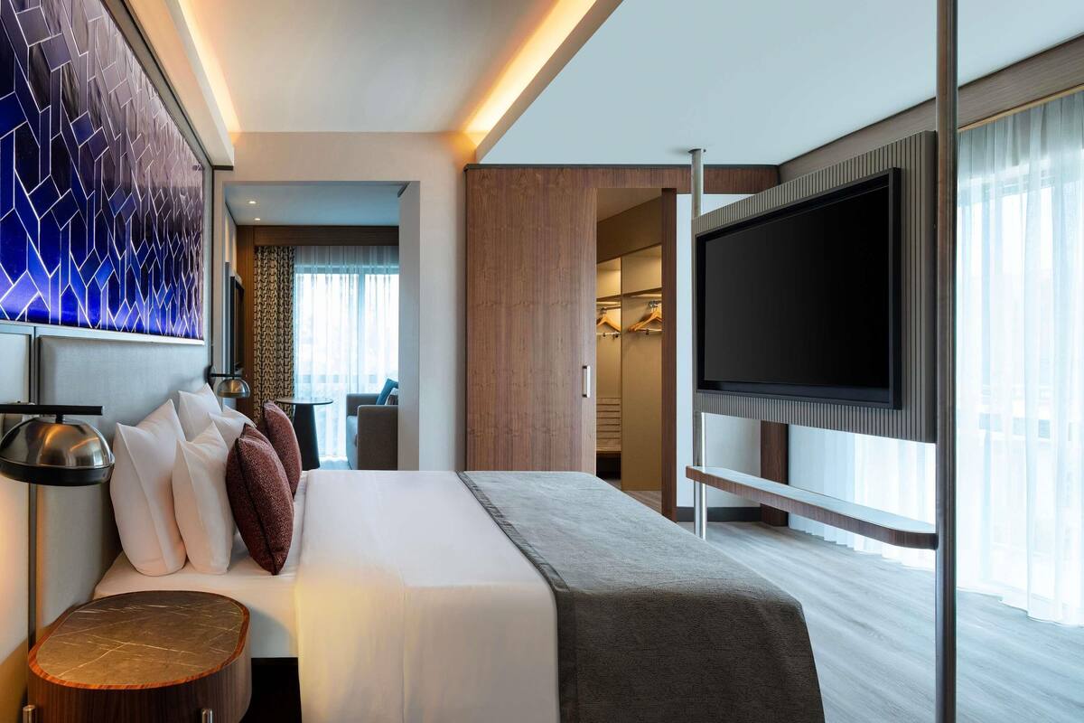 Een moderne hotelkamer met een bed, nachtkastje, televisie en uitzicht op de stad.