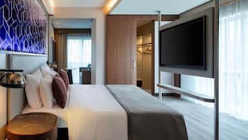 A modern hotel room with a bed, bedside table, TV, and a view of the city.